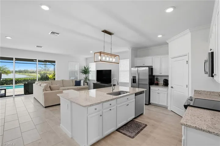 Kitchen with white cabinets, light stone countertops, hanging light fixtures, a center island with sink, and open floor plan