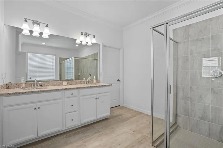 Bathroom featuring crown molding, a shower stall, and double vanity