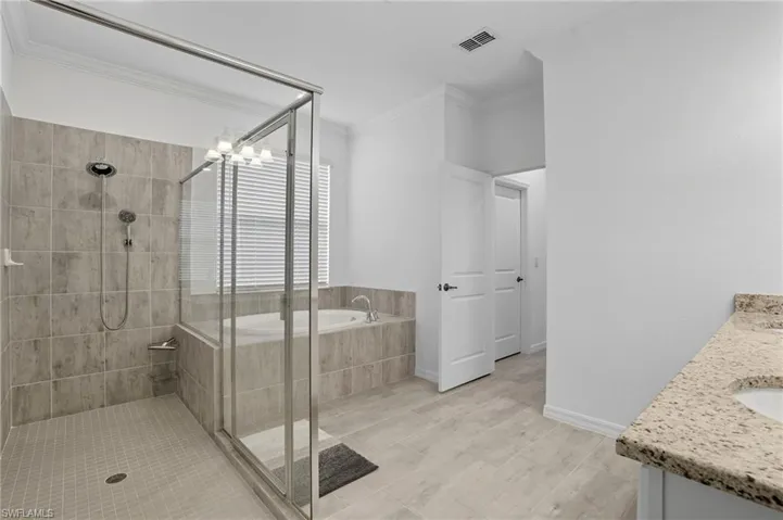 Bathroom featuring a shower stall, a garden tub, crown molding, double vanity, and a chandelier