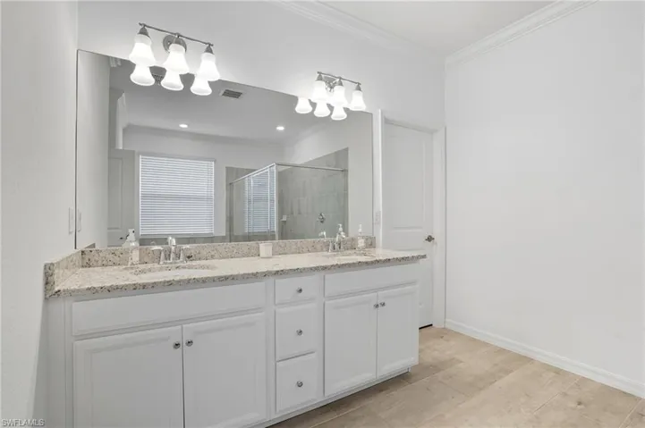 Full bathroom featuring crown molding, a shower stall, and double vanity
