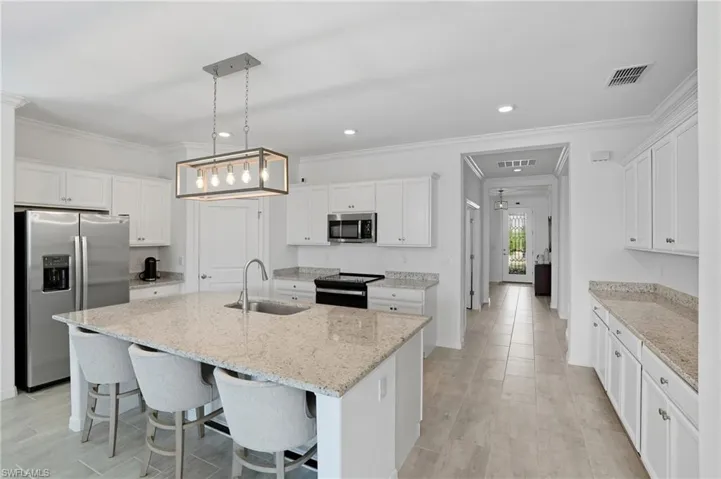 Kitchen with ornamental molding, appliances with stainless steel finishes, white cabinets, a kitchen breakfast bar, and hanging light fixtures