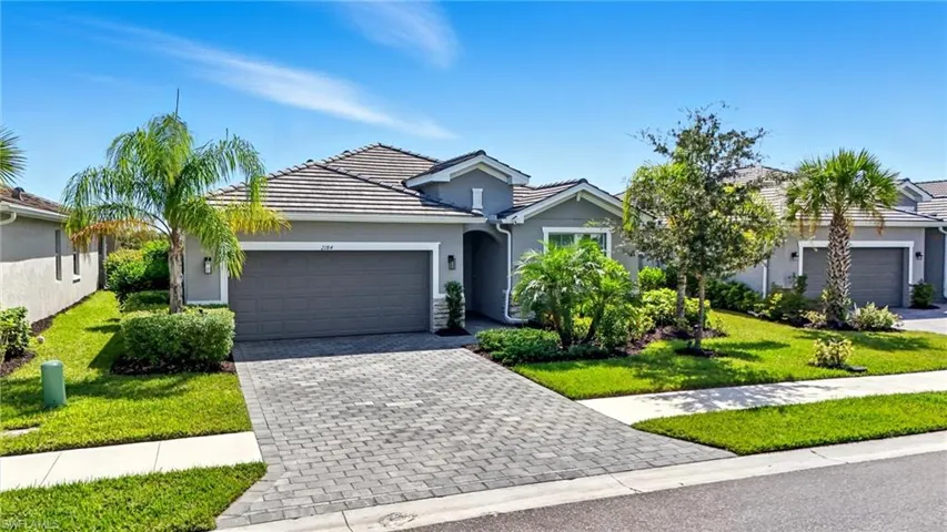 View of front facade with a front yard, decorative driveway, an attached garage, stucco siding, and a tile roof