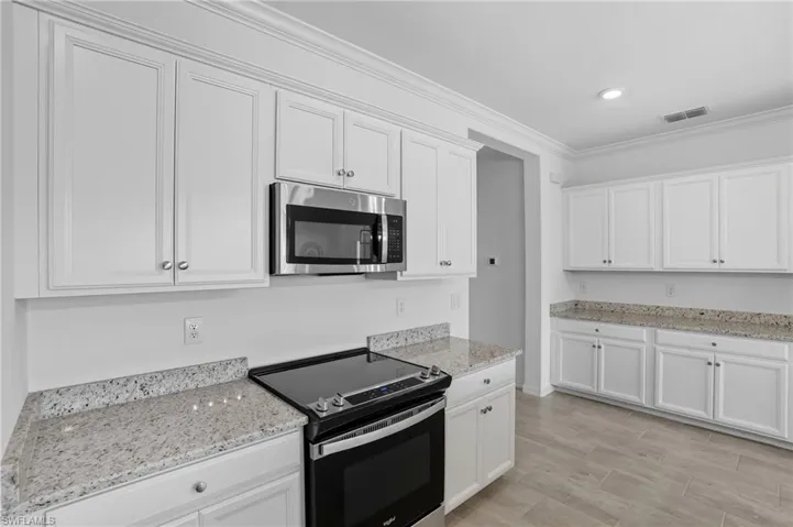 Kitchen featuring appliances with stainless steel finishes, crown molding, white cabinets, light stone counters, and wood finish floors