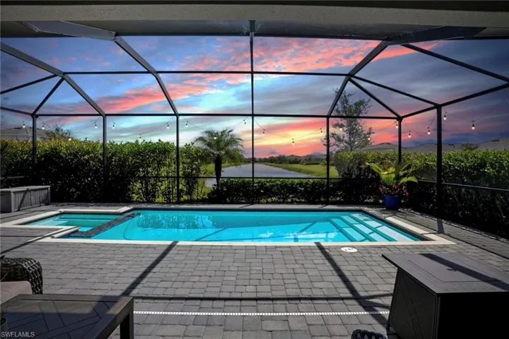 Pool at dusk with a sunroom, glass enclosure, a pool with connected hot tub, and a patio area