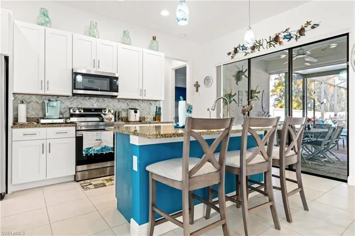 Dual tone kitchen featuring decorative light fixtures, a kitchen island with sink, stainless steel appliances, a breakfast bar area, and dark stone countertops