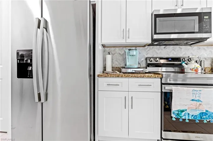 Kitchen featuring stainless steel appliances, white cabinetry, light stone counters, and backsplash