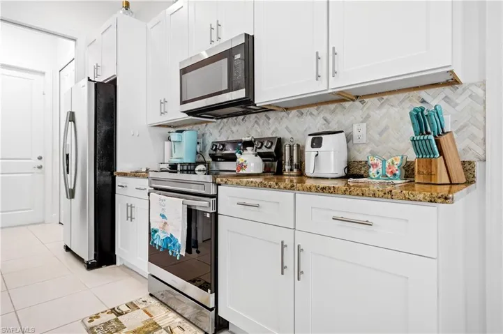 Kitchen featuring stainless steel appliances, white cabinets, dark stone counters, and light tile patterned flooring