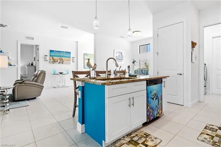 Kitchen with dark stone countertops, a breakfast bar area, dishwashing machine, open floor plan, and light tile patterned floors