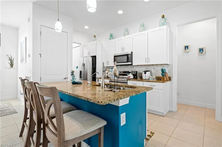 Kitchen featuring white cabinetry, hanging light fixtures, a kitchen bar, stainless steel appliances, and an island with sink