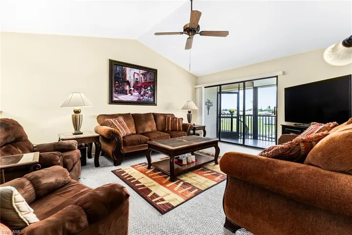 Living room with ceiling fan, light colored carpet, and lofted ceiling