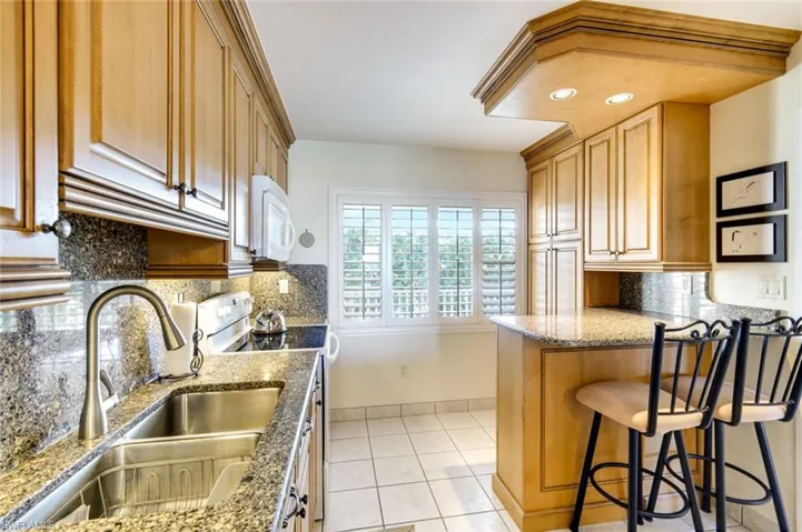 Kitchen featuring a kitchen bar, white appliances, light stone counters, light tile patterned floors, and a peninsula