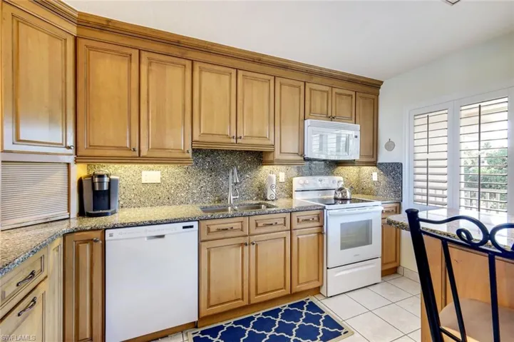 Kitchen featuring white appliances, brown cabinets, light tile patterned floors, tasteful backsplash, and light stone countertops