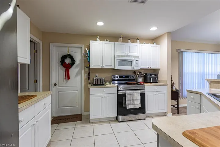 Kitchen featuring white cabinetry, light countertops, stainless steel electric range, light tile patterned floors, and white microwave