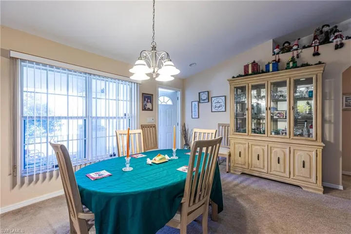 Dining room with light carpet, baseboards, lofted ceiling, and a chandelier