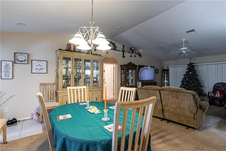 Tiled dining room featuring carpet flooring, lofted ceiling, ceiling fan with notable chandelier, visible vents, and arched walkways