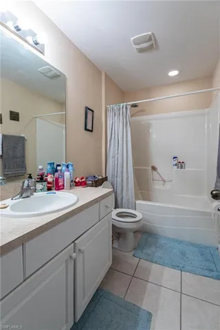 Bathroom featuring tile patterned flooring, vanity, shower / tub combo with curtain, toilet, and visible vents