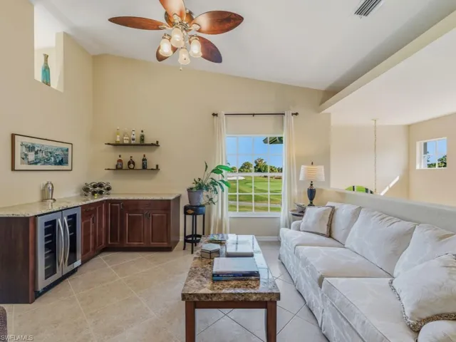 Open den/living area with wine cooler, a ceiling fan, bar with sink, lofted ceiling, and light tile patterned floors