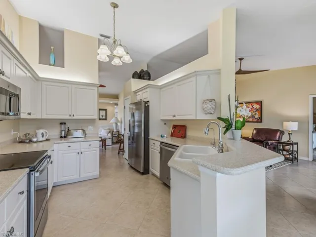 Kitchen with stainless steel appliances, a peninsula, white cabinets, open floor plan, and a towering ceiling