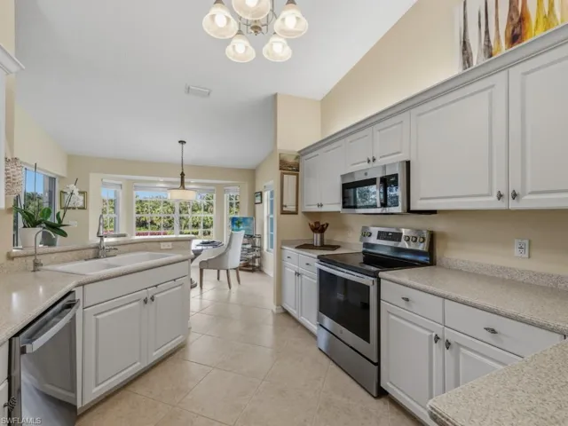 Kitchen with stainless steel appliances, decorative light fixtures, vaulted ceiling, a chandelier, and white cabinets