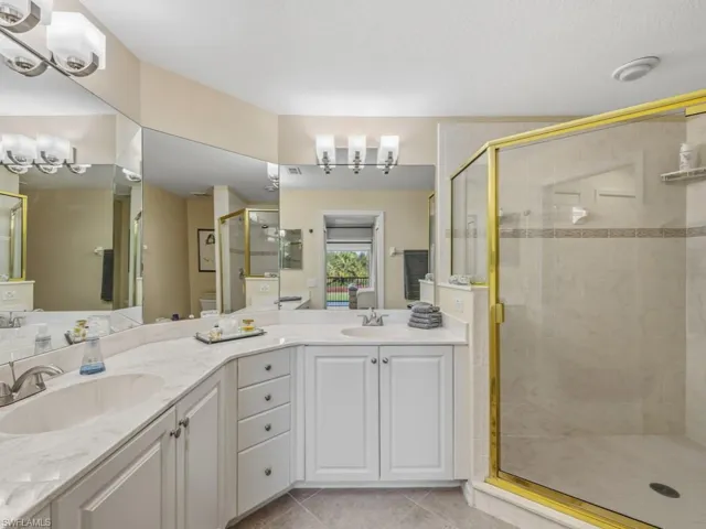 Full bathroom with double vanity, a stall shower, light tile patterned flooring, and a chandelier