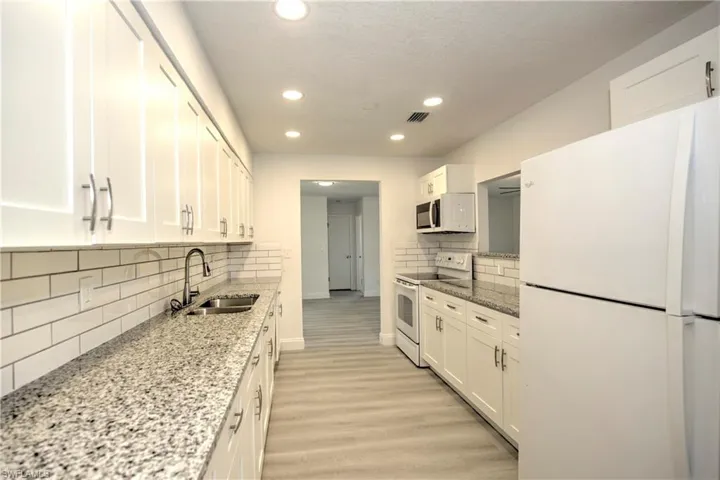 Kitchen featuring white appliances, light hardwood / wood-style flooring, white cabinetry, and sink
