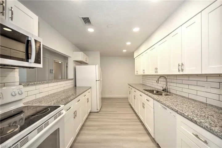 Kitchen with white appliances, white cabinets, sink, decorative backsplash, and light hardwood / wood-style floors