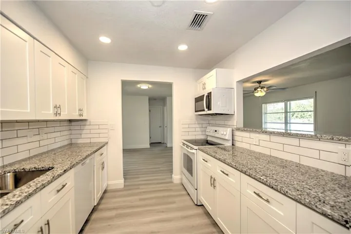 Kitchen with light stone countertops, white appliances, tasteful backsplash, and white cabinetry