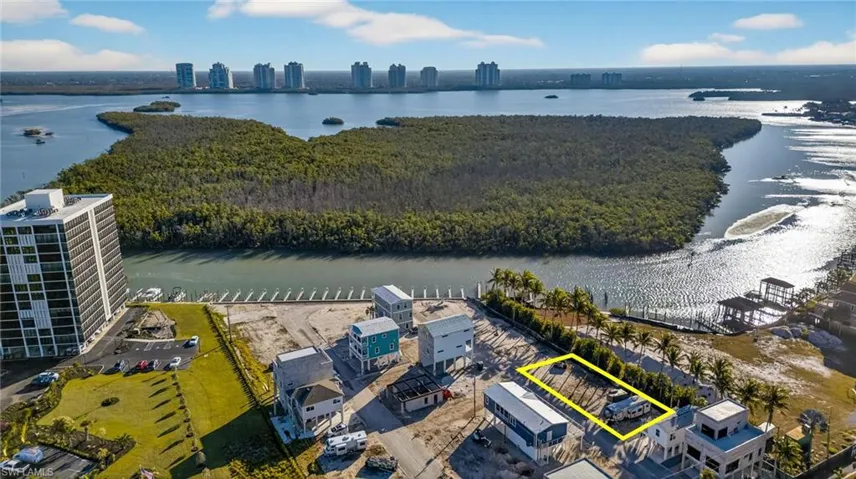 Aerial perspective of waterfront land parcel featuring cleared ground, palm tree landscaping, and proximity to a coastal waterway