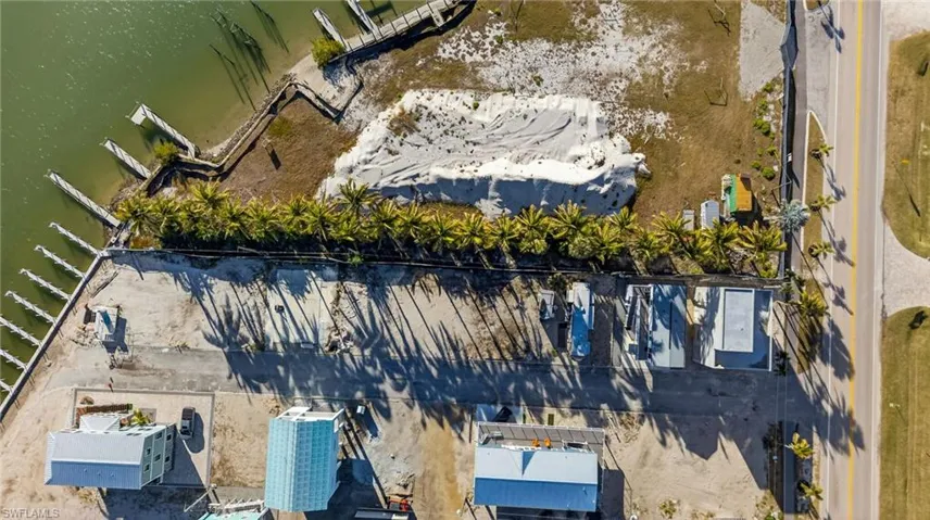 Waterfront lot featuring a sandy shoreline, multiple private boat docks, and a mature row of palm trees