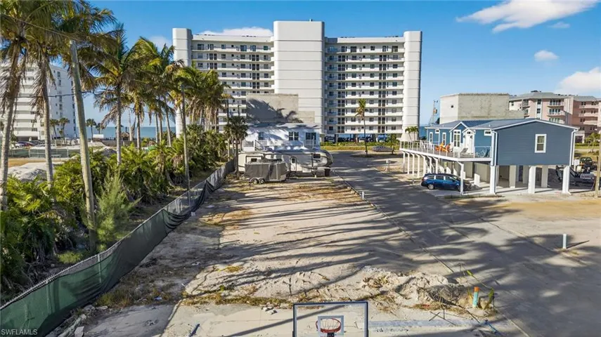 Vacant parcel featuring sandy ground, established palm trees, and perimeter privacy fencing