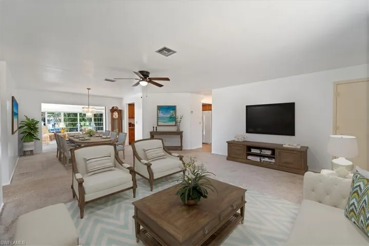 Living room featuring light carpet, visible vents, and ceiling fan with notable chandelier