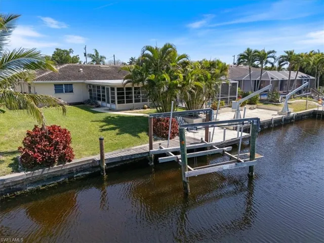 View of dock featuring glass enclosure, a water view, boat lift, and a lawn