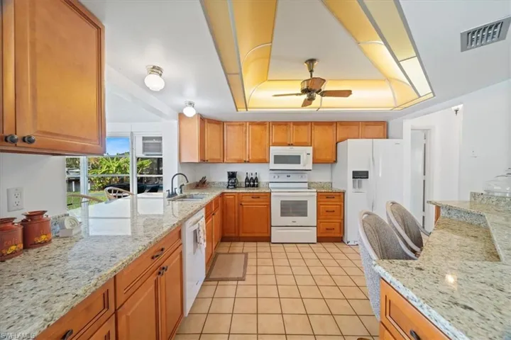 Kitchen with visible vents, light stone counters, white appliances, a raised ceiling, and ceiling fan