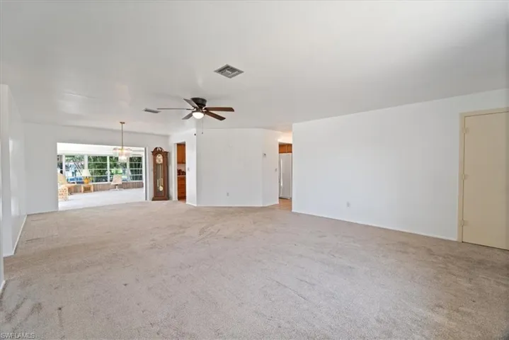 Unfurnished living room featuring light carpet, visible vents, and ceiling fan with notable chandelier