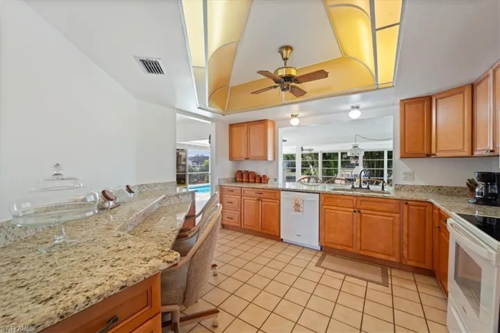 Kitchen featuring white appliances, light stone counters, visible vents, a sink, and a raised ceiling