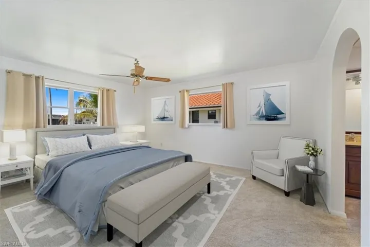Bedroom featuring baseboards, arched walkways, ornamental molding, ceiling fan, and light colored carpet