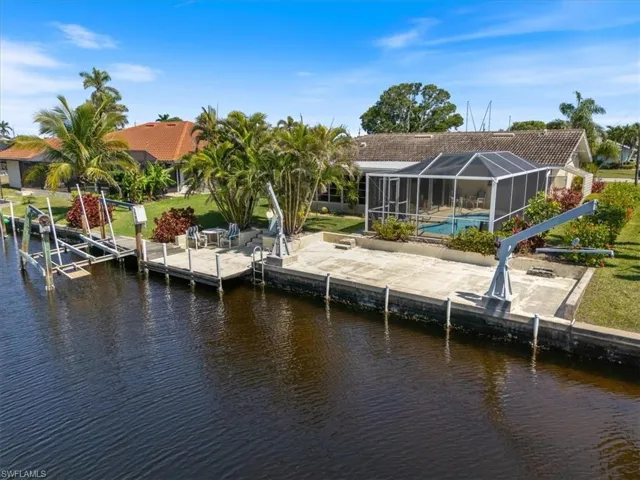 Dock area with a water view, glass enclosure, a patio area, boat lift, and an outdoor pool