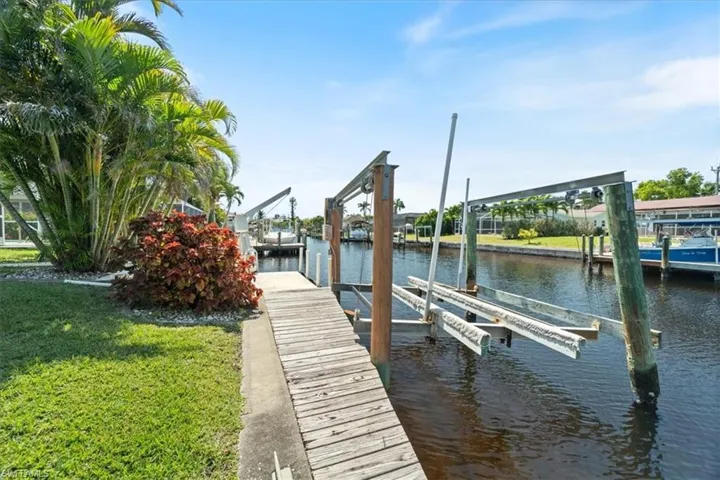 View of dock featuring a water view, boat lift, and a lawn