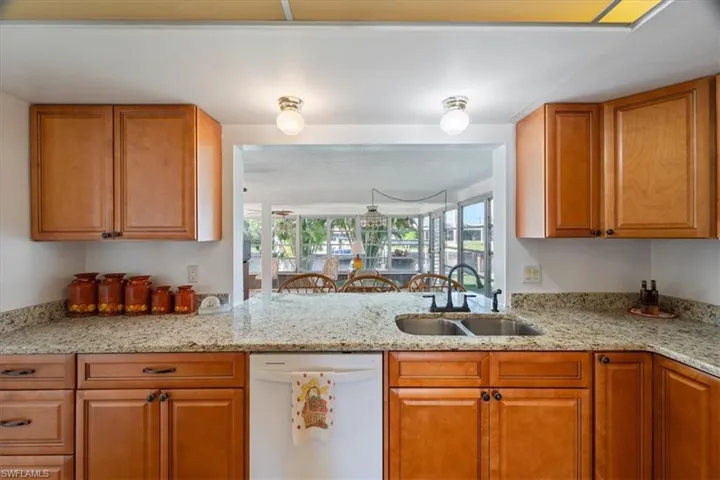 Kitchen featuring brown cabinetry, white dishwasher, light stone countertops, and a sink