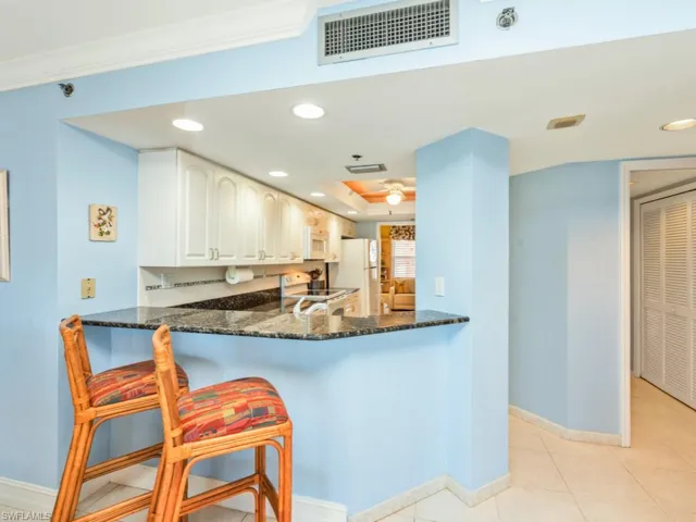 Kitchen featuring dark stone counters, a kitchen bar, white cabinetry, white appliances, and light tile floors