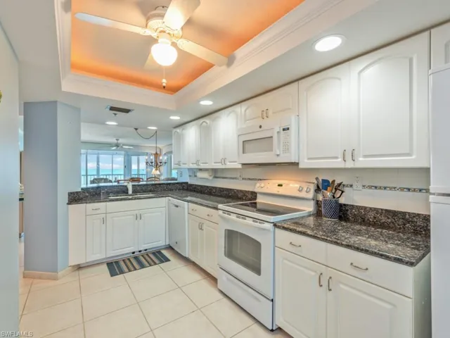 Kitchen with ornamental molding, a tray ceiling, white appliances, white cabinets, and ceiling fan