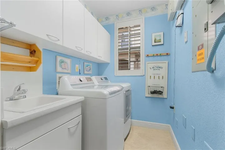 Washroom featuring cabinet space, electric panel, washer and dryer, and light tile patterned floors