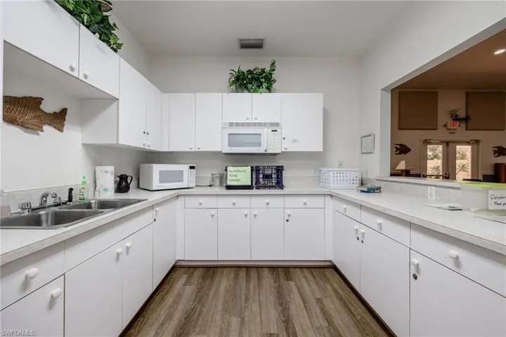 Community kitchen featuring white microwave, light countertops, dark wood finished floors, and white cabinetry