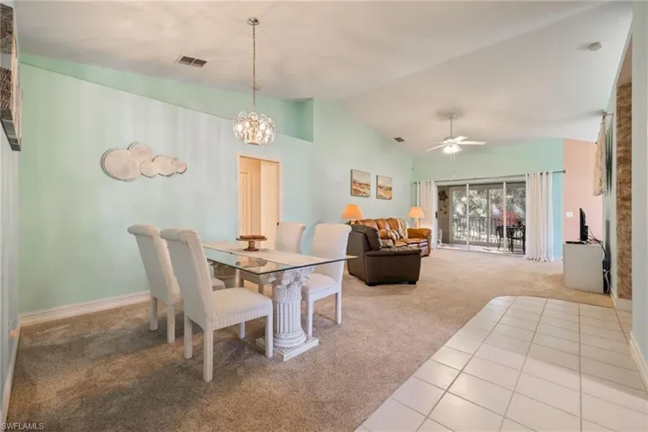 Carpeted dining area featuring a ceiling fan, a chandelier, high vaulted ceiling, and tile patterned flooring