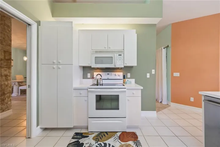 Kitchen featuring white appliances, light countertops, white cabinets, and light tile patterned floors