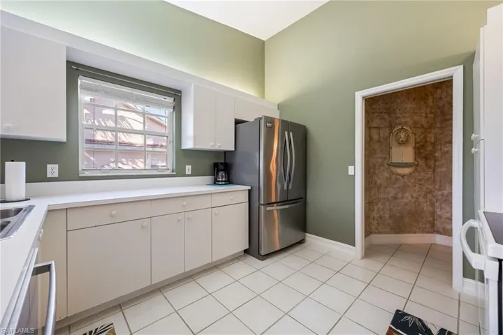 Kitchen with refrigerator, white range oven, light countertops, white cabinets, and light tile patterned flooring