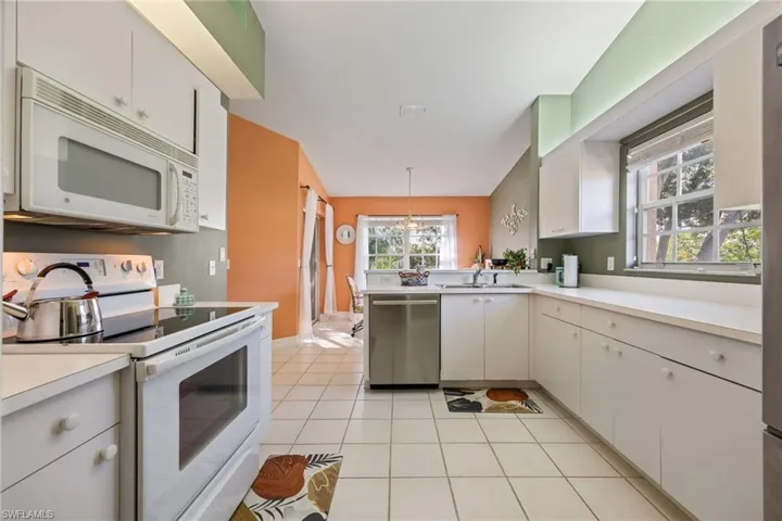 Kitchen with white appliances, light countertops, a peninsula, light tile patterned flooring, and hanging light fixtures