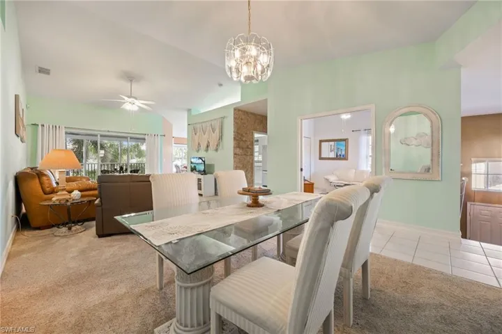 Dining space with healthy amount of natural light, light tile patterned floors, a chandelier, light carpet, and vaulted ceiling