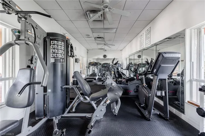 Community workout area featuring a drop ceiling, a ceiling fan, and plenty of natural light