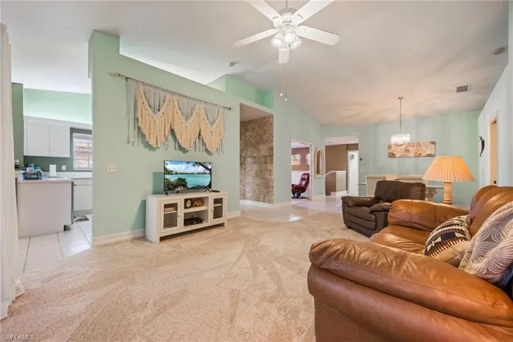 Living area featuring light tile patterned flooring, vaulted ceiling, a ceiling fan, light colored carpet, and a chandelier